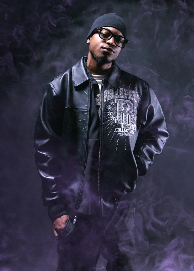 Model wearing a black leather-style streetwear jacket with silver embroidered Collectors Series chest graphics, a bold decorative emblem, and ribbed cuffs against a dark smoky background.